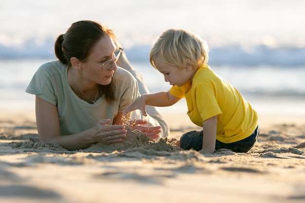 Little blonde boy and his mother playing with the sand