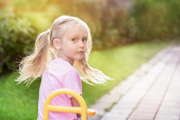 Little blonde european girl rides a bike in the park on a sunny summer day