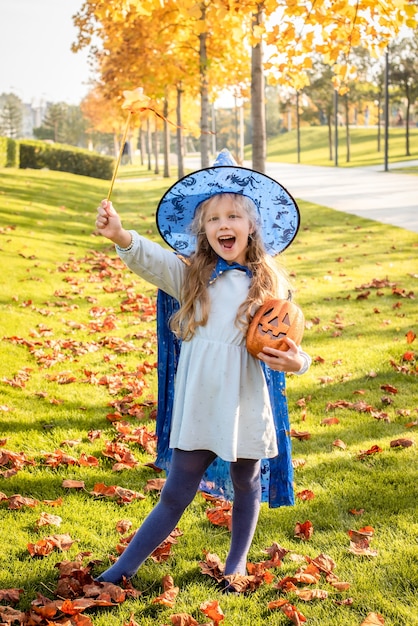 Little blonde girl dressed as a witch, wizard for halloween. hat, cloak, pumpkin, laugh, smile, autumn holiday