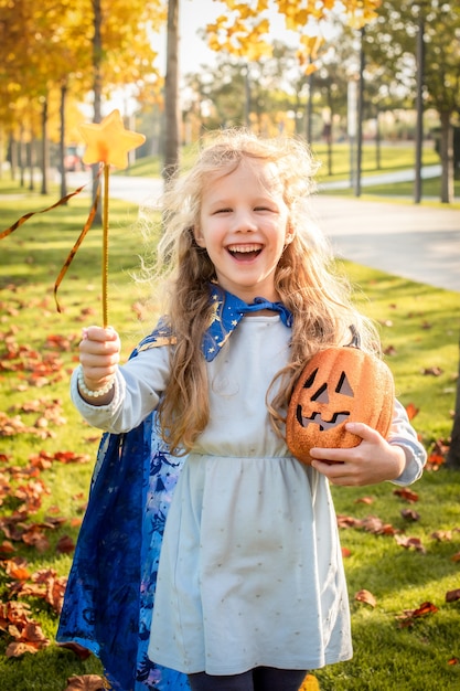 Little blonde girl dressed as a witch, wizard for halloween. hat, cloak, pumpkin, laugh, smile, autumn holiday