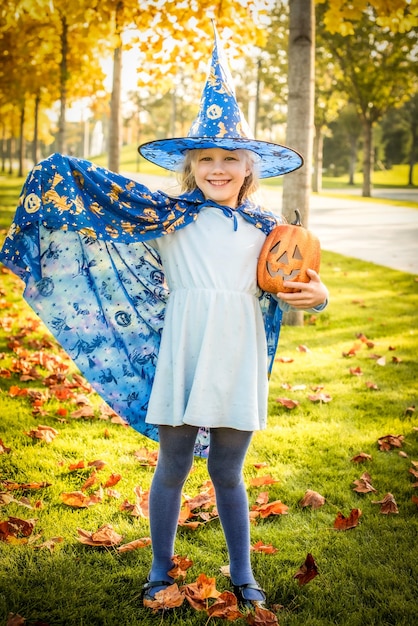 Little blonde girl dressed as a witch wizard for halloween hat cloak pumpkin laugh smile autumn holiday