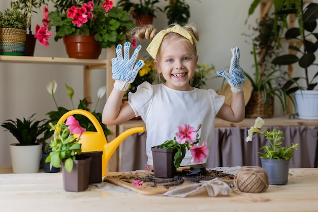 little blonde girl of European appearance with a bow on head and wearing work gloves plants flowers