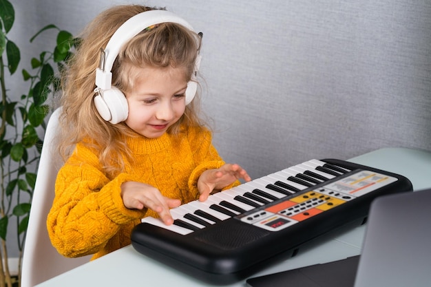 A little blonde girl in headphones smiling and playing the synthesizer the concept of teaching children music