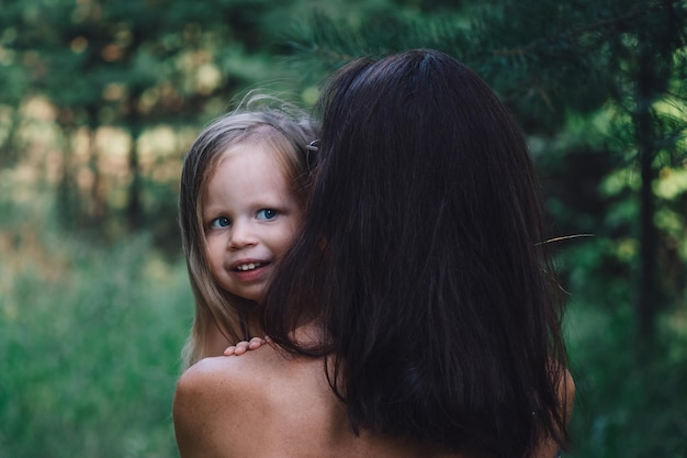 A little blonde girl in her mother's arms closeup Portrait of a beautiful happy smiling girl Happy childhood family love concept Mom holds a child in her arms in nature in forest park