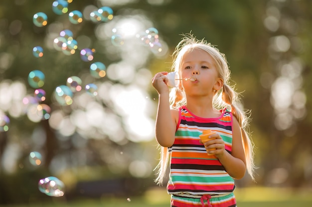 little blonde girl inflates soap bubbles in summer on a walk