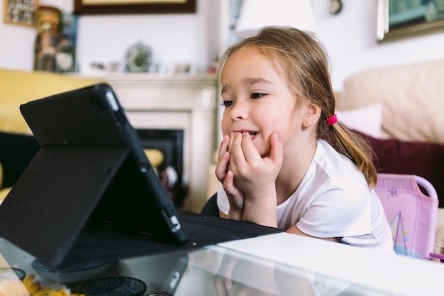 A little blonde girl intently watching a video on a tablet in her living room Concept of childhood technology learning having fun the Internet and connectivity