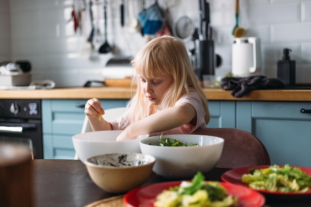 Little blonde girl is helping to prepare dinner in the kitchen