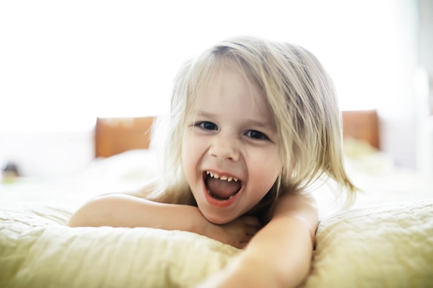 Little blonde girl lies on the bed Emotional child infant posing