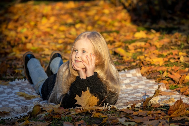 Little blonde girl lies on a blanket in the park in autumn