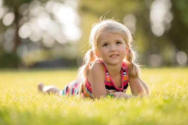 little blonde girl lying on the green grass smiling