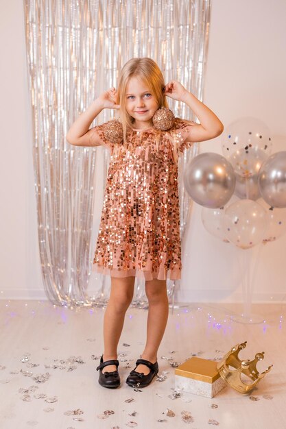 a little blonde girl in a shiny dress plays with Christmas balls at the New Year's carnival