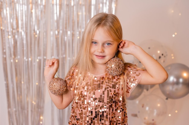 a little blonde girl in a shiny dress plays with Christmas balls at the New Year's carnival