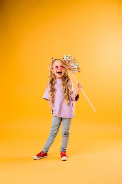 little blonde girl smiling in sunglasses holding a windmill stands on a yellow space