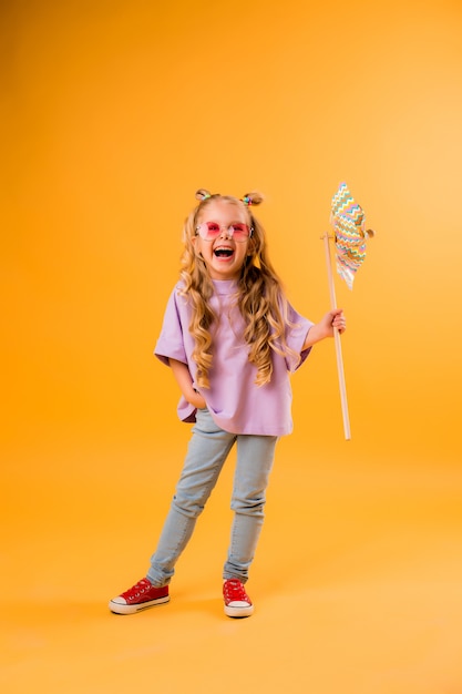 little blonde girl smiling in sunglasses holding a windmill stands on a yellow space