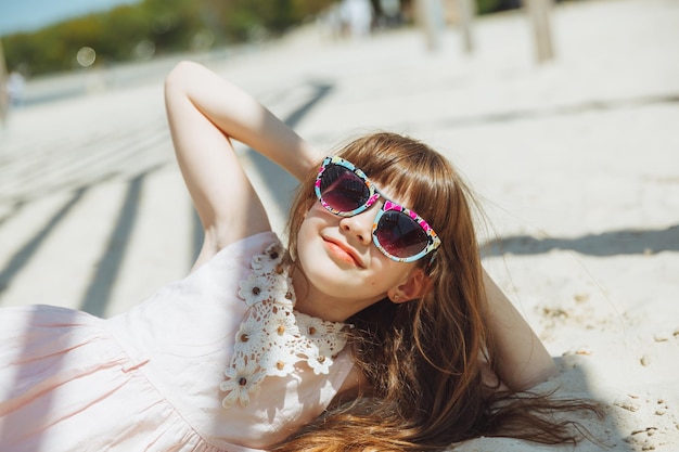 A little blonde girl in a straw hat lies on a sandy beach girl sunbathing on the sand