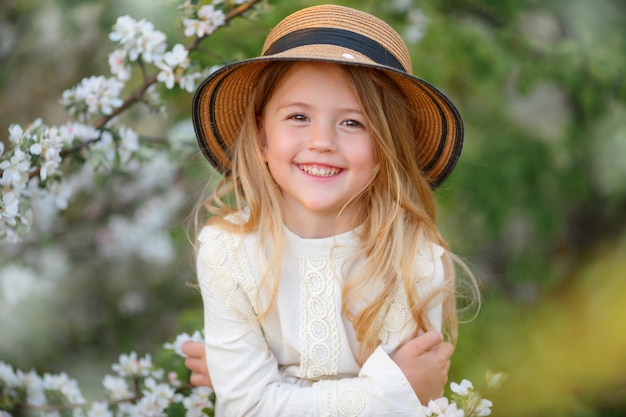 Little blonde girl in a straw hat near a flowering tree