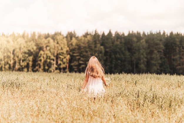 A little blonde girl walks through a golden field in the summer. Concept of purity, growth, happiness