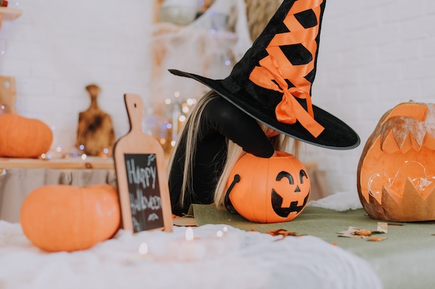 little blonde girl in a witch costume takes out or puts sweets in a basket in the shape of a pumpkin