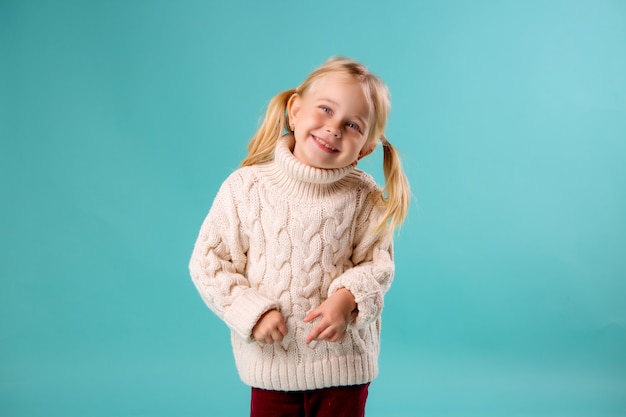 little blonde in sweater smiling on blue