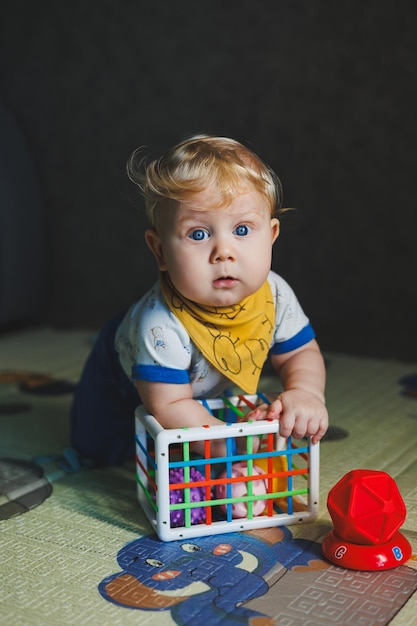 A little boy of 6 months sits on a developmental mat and plays with a sorter with balls educational games for babies Development of hand motility in children