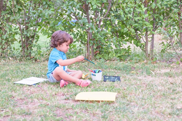 Little boy are using a magic pen to draw pictures in a book on a wooden table in park With face expression of determination