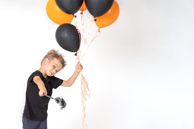 A little boy in a black Tshirt holding a magic wand and orange and black balloons conjures on a white background