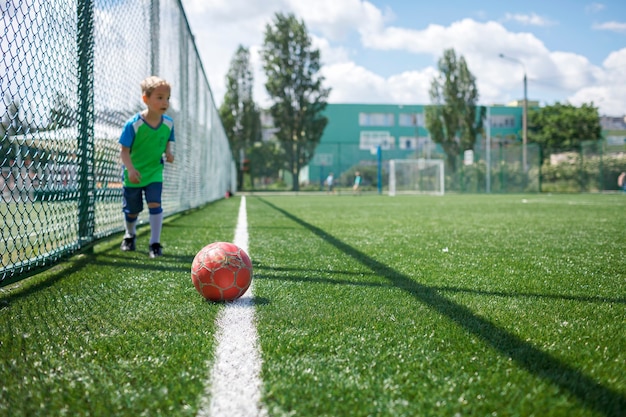 Little boy in blue and green form playing football on open field in the yard a young soccer player