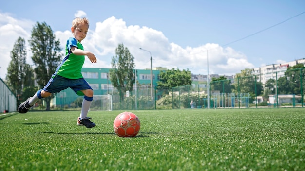 Little boy in blue and green form playing football on open field in the yard a young soccer player