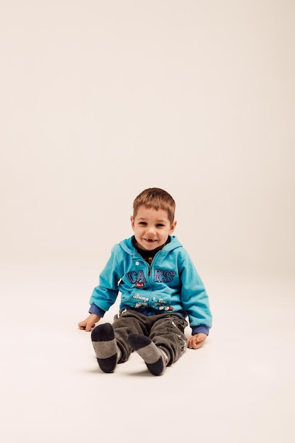 A little boy in a blue jacket sits on a white background