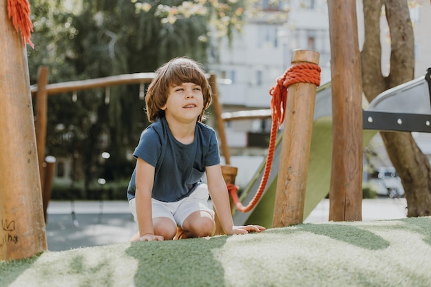 Little boy in a blue T-shirt and white shorts is sitting on the green grass on the playground. child actively spends time playing and walking outdoors. lifestyle. space for text. High quality photo