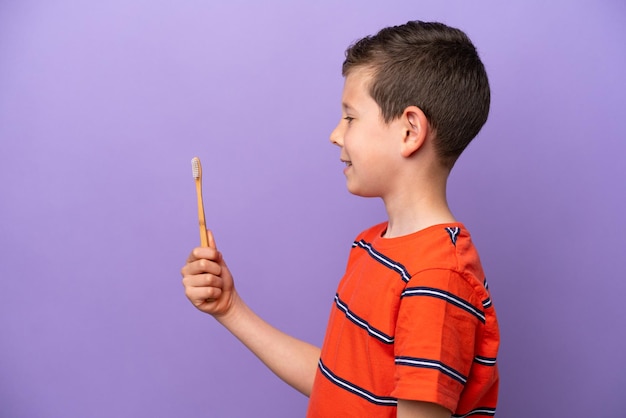 Little boy brushing teeth isolated on purple background with happy expression