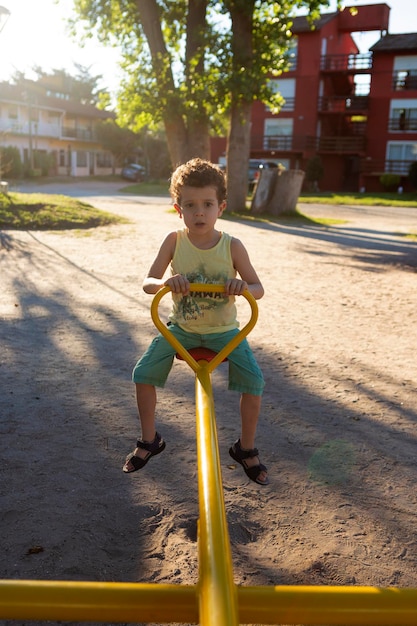 Little boy of Caucasian appearance with curly hair riding on a seesaw in the park