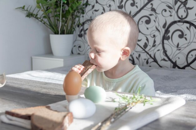 A little boy celebrates Easter sits at a wooden table and eats