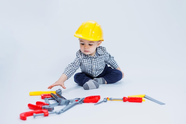 A little boy in a checkered shirt in the image of a builder A boy in a construction helmet and plastic tools