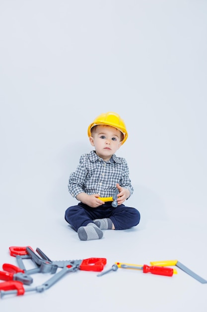 A little boy in a checkered shirt in the image of a builder A boy in a construction helmet and plastic tools