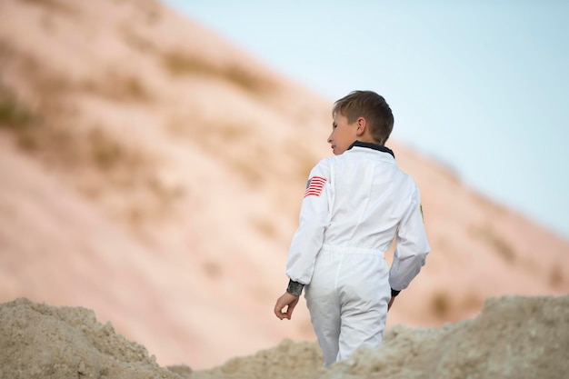 A little boy dressed as an American astronaut walks through exotic mountains of white sand