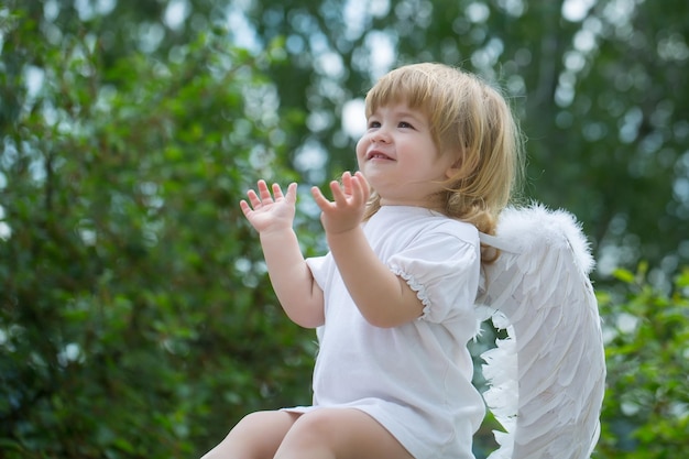 Little boy dressed as angel claps his hands happy cupid on the chair