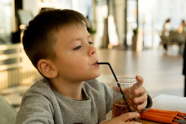 Little boy drink juice from glasses through straws in city cafe. Lifestyle concept.