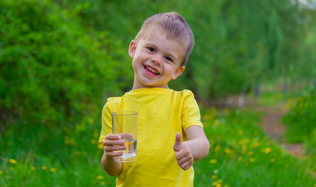 Little boy drinking water with a glass in the park