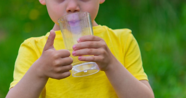 Little boy drinking water with a glass in the park