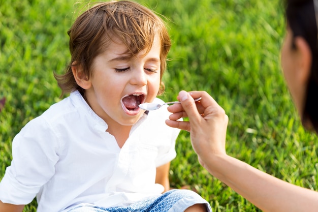 The little boy eating yogurt in the park.