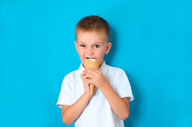 A little boy eats ice cream in a cone on a blue background with free space for copying text