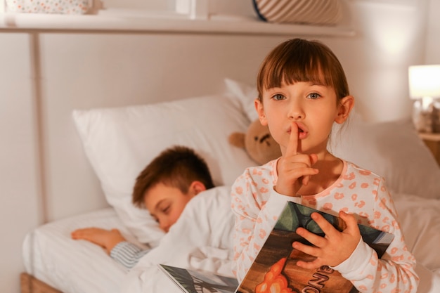 Little boy falling asleep while his sister reading bedtime story at home