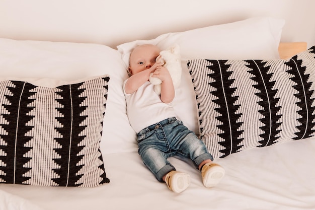 Little boy funny cute child baby lying on bed pillows with fluffy toy. Playful toddler