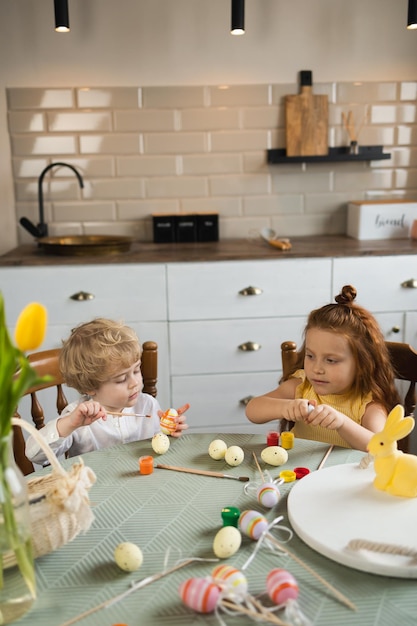 Little boy and girl paint Easter eggs in the kitchen