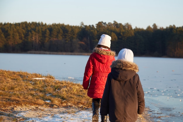 Little boy and girl walking near river in sunny winter day.