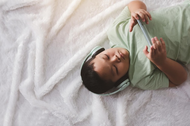 The little boy happily lies down and listens to music with headphones.