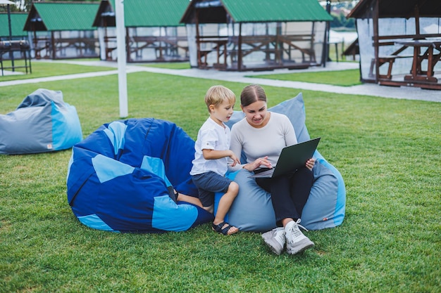 Little boy having fun sitting on sack in summer or spring in park outdoors Family vacation of mother and son in the fresh air