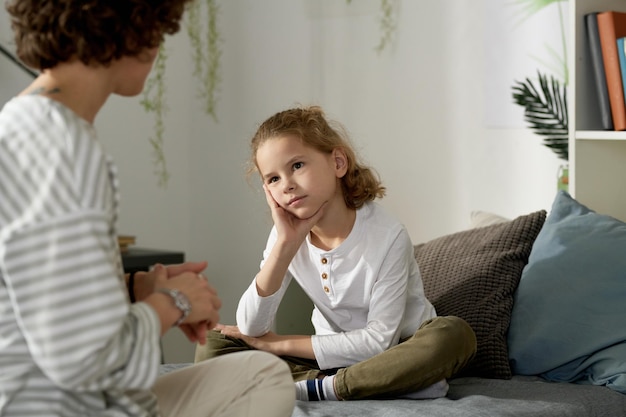 Little boy having serious conversation with his mom while sitting on bed in his bedroom