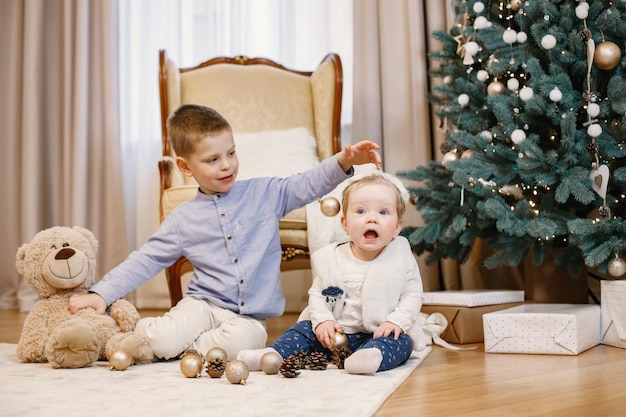 Little boy and his sister sitting near christmas tree at home